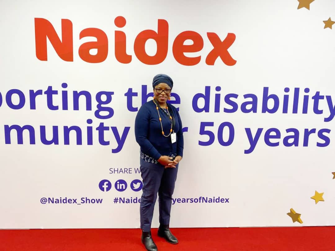 Funmi Lawal Standing In Front Of A Naidex Background. She Is Wearing A Blue Trousers, Blue Blouse And A Blue Cardigan.