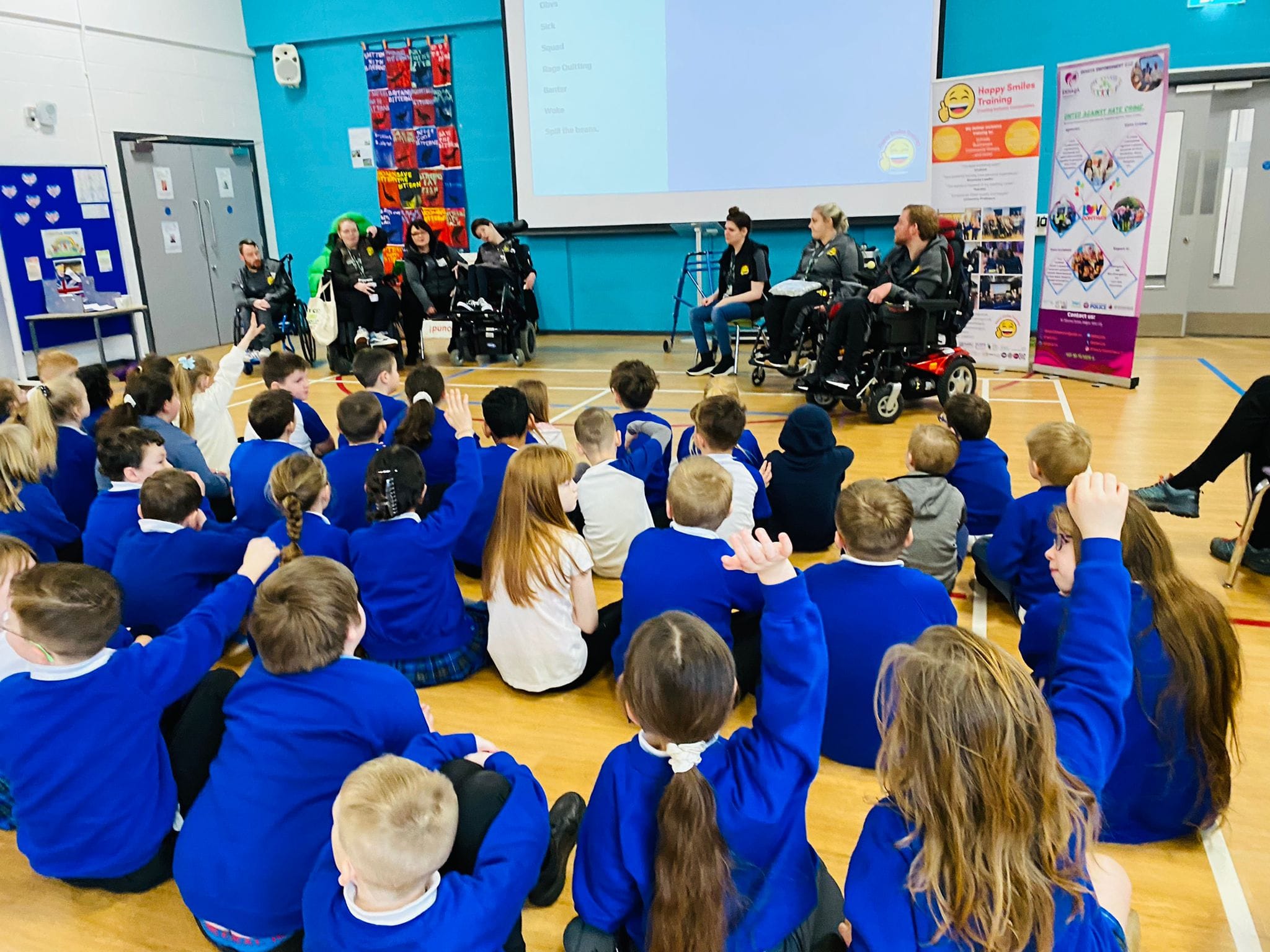 A class of school pupils listening to members of the Happy Smiles team, with some raising their hands.